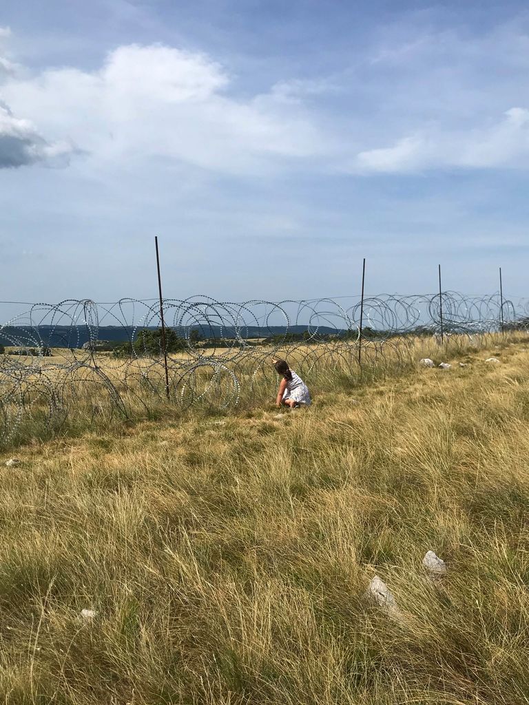 Campo con ragazza accovacciata sotto il filo spinato